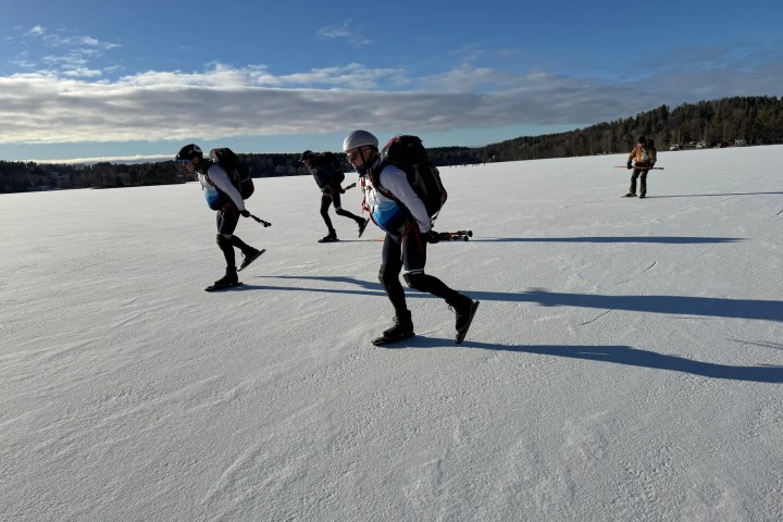 Four people ice skating on a frozen lake under a cloudy sky.